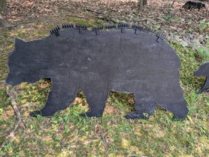 Black plywood silhouette of a bear, with three spike strips mounted on top.
