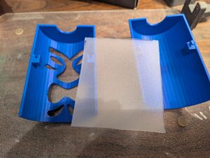 Close-up of the two halves of a blue shade with the diffuser sheet that will be mounted inside. The fasteners are clearly visible inside the two halves. 