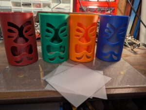 The front halves of four printed tiki heads, each a different color, with cut plastic diffuser sheets in front of them.