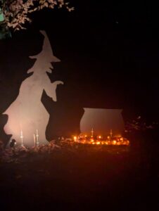 The witch, cauldron, and "lit" coals (LED lights lit), seen at night. The silhouettes are lit by a spotlight.
