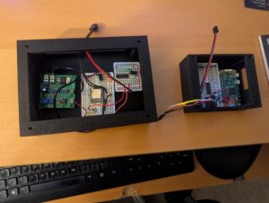 Photo of the electronics for the skeleton in one project box and the pi-based multi-prop controller in a second project box. The skeleton controller has a Jemmy Talk circuit board, a board with the MP3 player, and a third board. The prop controller has a raspberry pi and a board with a Darlington array, source for power, and several female 3-pin headers.